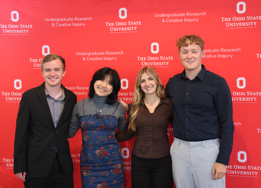 Four people smiling and standing in front of a backdrop
