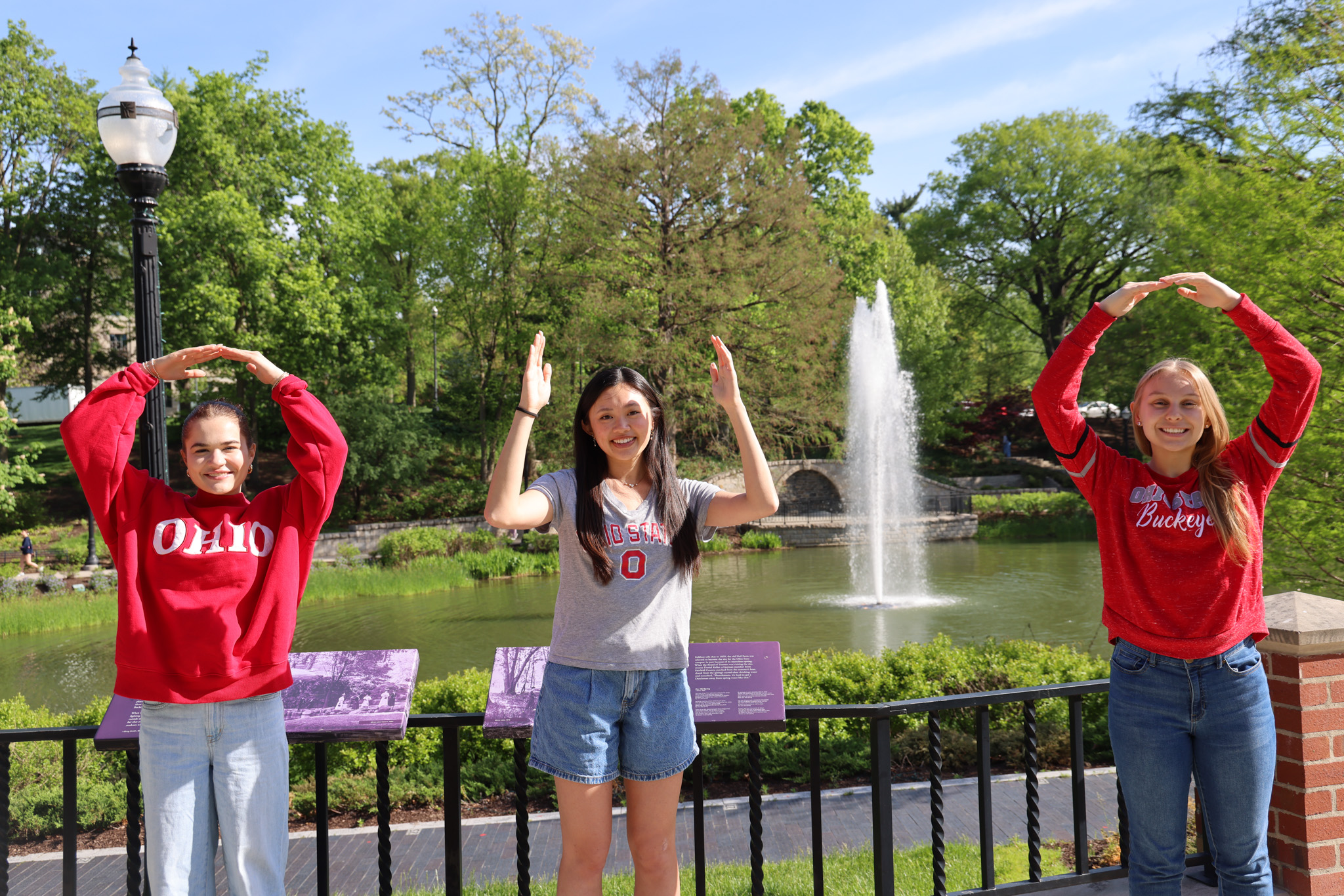 Three individuals spell out "OHIO" with their arms with the mirror lake fountain in the background