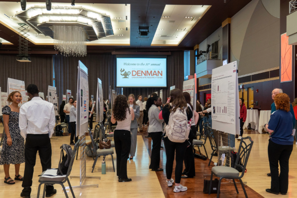 A conference hall features several people viewing and discussing research posters.