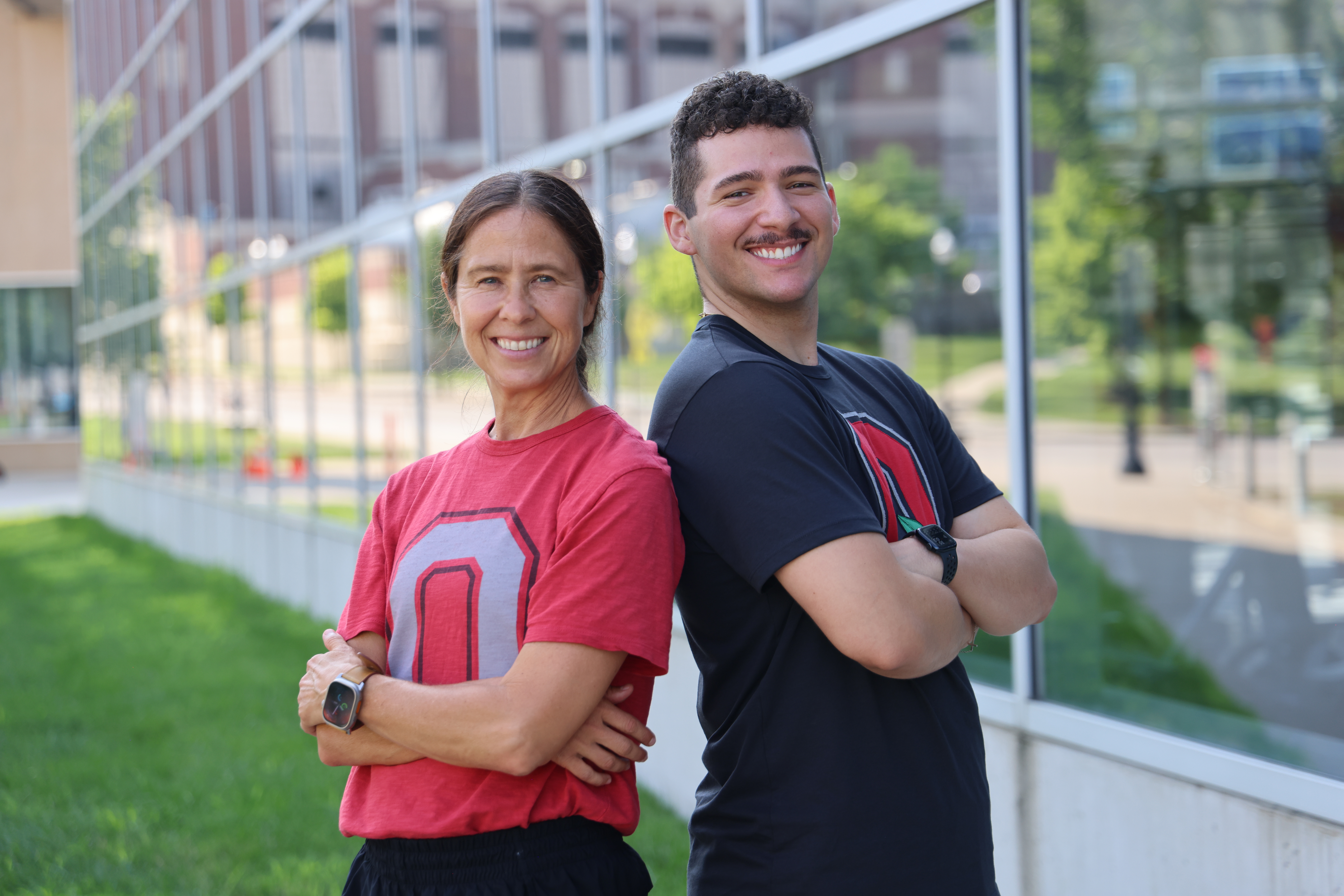 Two individuals are standing back-to-back, smiling and wearing t-shirts featuring a large letter "O."