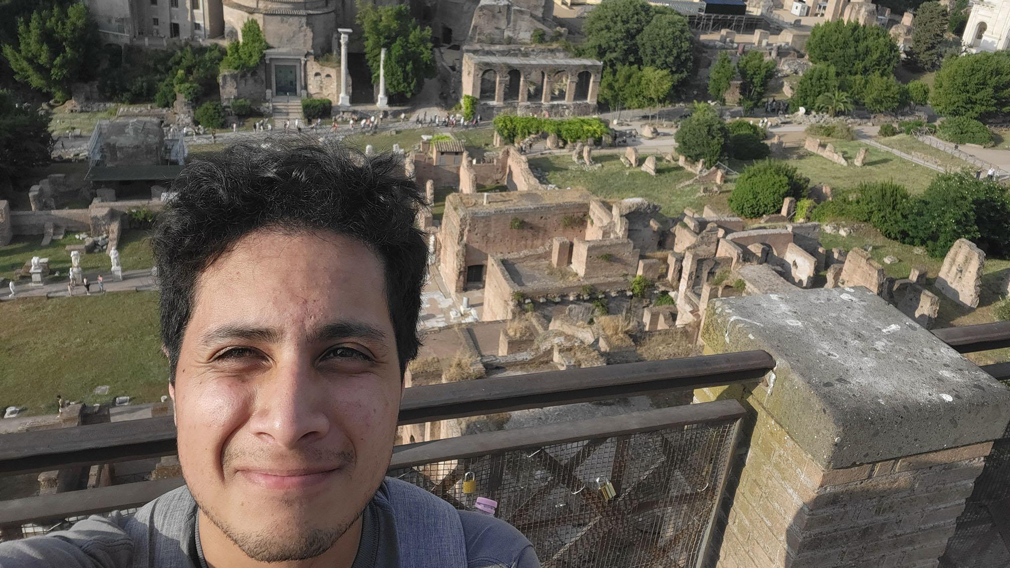 A person is taking a selfie with a view of ancient ruins in the background.