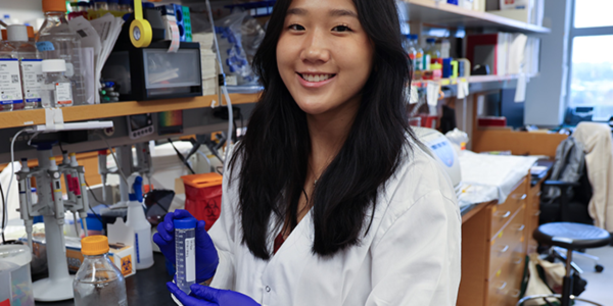 A person wearing a lab coat and gloves holds a test tube in a laboratory. 
