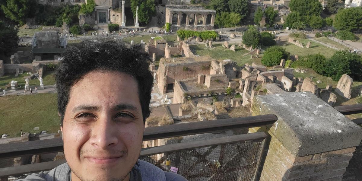 A person is taking a selfie with a view of ancient ruins in the background.