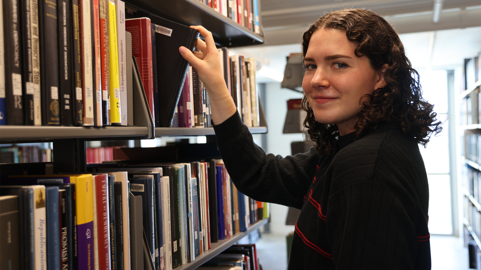 Ohio State student smiling as she grabs a book in the library